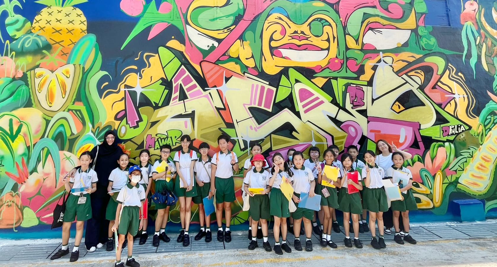 Students and teachers pose for a group photo in front of a vibrant mural during a learning journey, celebrating art, culture and shared learning experiences.